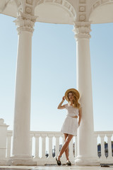 Wall Mural - blonde girl stands cross-legged in a gazebo of stone white columns