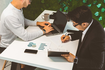 Young office worker sitting at desk, using computer. Two business man talking