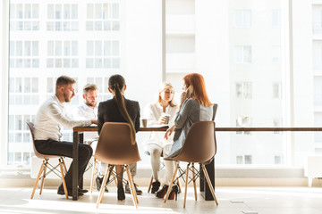 Wall Mural - A team of young businessmen working and communicating together in an office. Corporate businessteam and manager in a meeting. desktop against the background of the pan window, free space for text