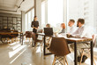 © xartproduction - A team of young businessmen working and communicating together in an office. Corporate businessteam and manager in a meeting. desktop against the background of the pan window, free space for text