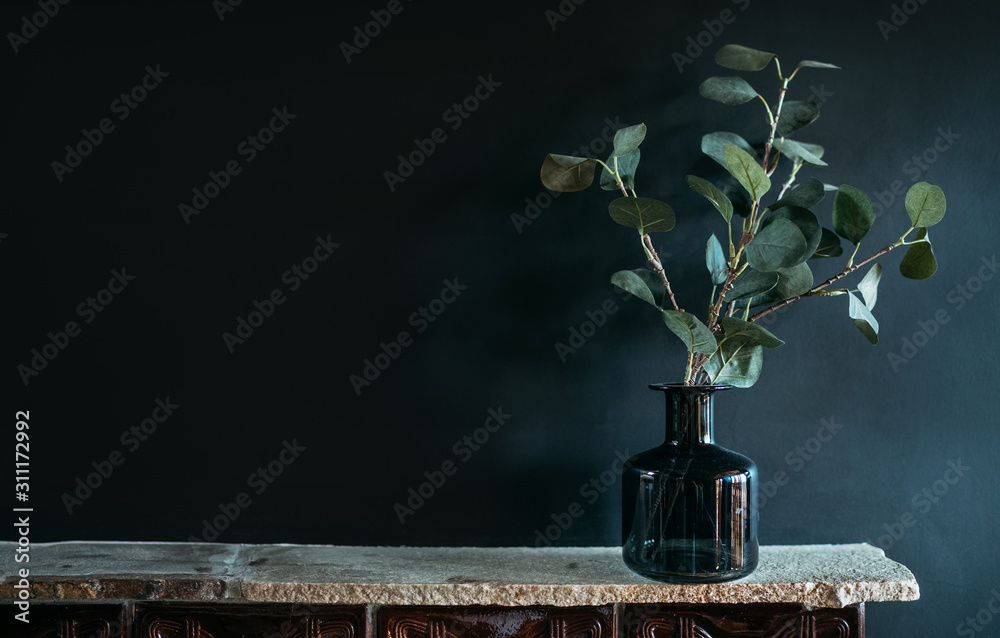 Obraz na płótnie Green tree Branch putted into black glass vase on the natural stone mantel shelf on the black color wall background lit with side window light. Cozy home decor elements concept image. w salonie