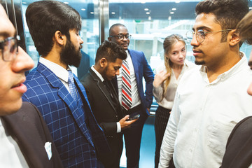 Sticker - Business team group going on elevator. Business people in a large glass elevator in a modern office. Corporate businessteam and manager in a meeting.