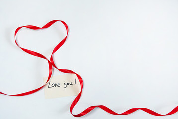 The concept of Valentine's Day in the style of minimalism. The border is made of red silk ribbon and a note with a Declaration of love on a white background. Free space for your text.