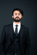 © xartproduction - Portrait of a young handsome successful Indian in a classic black three-piece business suit on a dark background, hold down the glasses