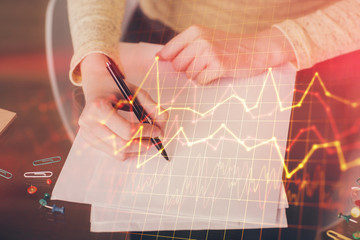 Hand taking notes in notepad. Forex chart holograms in front. Concept of research. Multi exposure