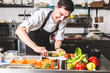 © xartproduction - Professional chef cooking in the kitchen restaurant at the hotel, preparing dinner. A cook in an apron makes a salad of vegetables and pizza.