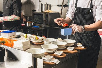 Wall Mural - Professional chef cooking in the kitchen restaurant at the hotel, preparing dinner. A cook in an apron makes a salad of vegetables and pizza.