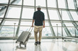 © Nopphon - A male traveler wearing a gray hat Preparing to travel He has a trolley bag He stands at a large airport for traveling around the world.