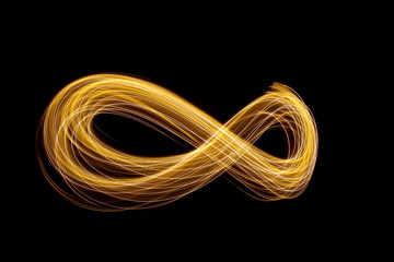 Wall Mural - Long exposure photograph of an infinity loop in gold neon colour in an abstract swirl, parallel lines pattern against a black background. Light painting photography.