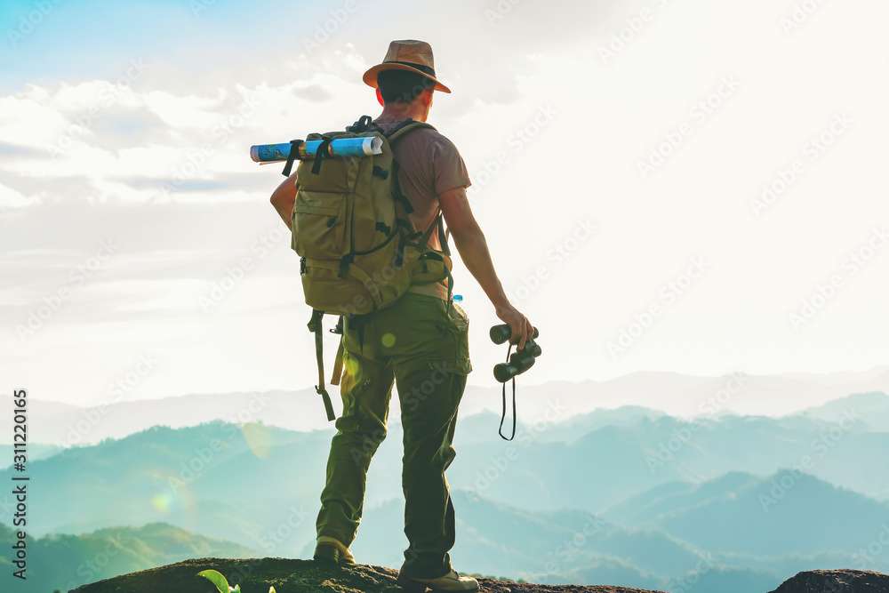The hiker with a backpack stood on the rock after examining the map to find a path in a beautiful mountain landscape. - obrazy, fototapety, plakaty 