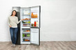 © New Africa - Happy young woman near open refrigerator indoors, space for text