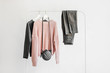 Female clothes in pastel pink and gray color on hanger on white background.  Jumper, shirt, jeans and bag. Spring/autumn outfit. Minimal concept.