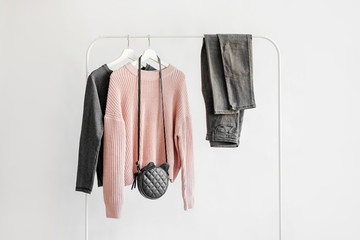 Wall Mural - Female clothes in pastel pink and gray color on hanger on white background. Jumper, shirt, jeans and bag. Spring/autumn outfit. Minimal concept.