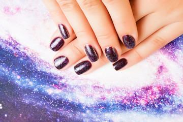 manicure stylish concept: woman fingers with nails purple glitter on nails like cosmos, universe background