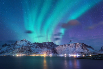 aurora borealis over the sea, snowy mountains and city lights at night. northern lights in lofoten i