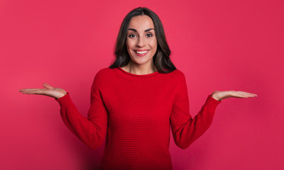 Two sides. Close-up photo of an attractive woman in a ruby red sweater, who is looking in the camera, smiling and imitating scales with her hands.