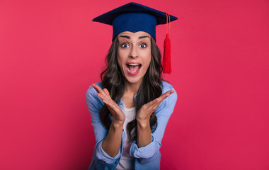 On the top of the world. Close-up photo of a lovely student in a casual outfit and a student cap, who is posing with her palms opened near her chest and screaming with happiness for her success.