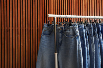 Poster - Rack with different jeans on wooden background, closeup. Space for text