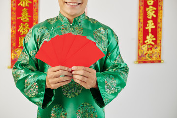 Poster - Cropped image of happy Asian man holding many red envelopes for Lunar New Year celebration