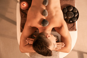 Poster - Handsome man undergoing treatment with spa stones in beauty salon, top view