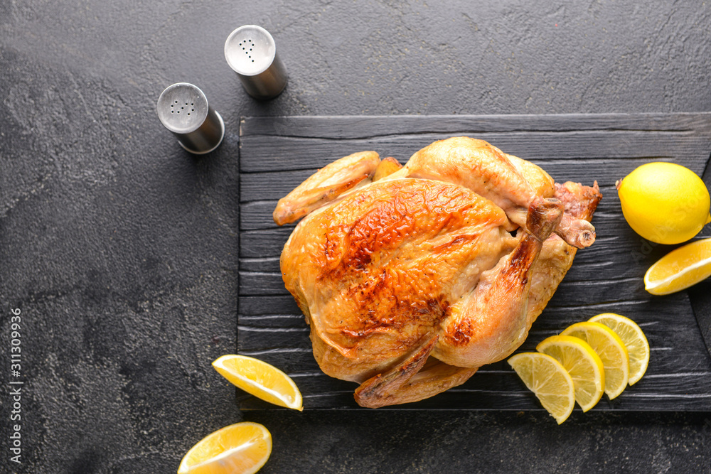 Board with baked chicken on dark background