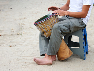 A man plays an African jamba drum, an ethnic musical instrument. He is on the seashore, sitting on the sand with bare feet. Creativity, rest and relaxation.