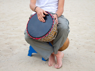 Wall Mural - A man plays an African jamba drum, an ethnic musical instrument. He is on the seashore, sitting on the sand with bare feet. Creativity, rest and relaxation.