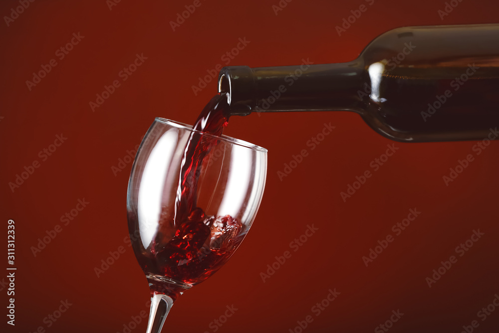 Pouring of wine into glass on color background