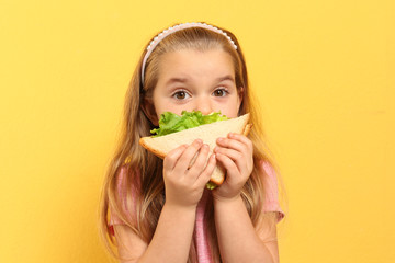 cute little girl eating tasty sandwich on yellow background