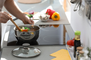 Canvas Print - Young man cooking delicious soup in kitchen, closeup