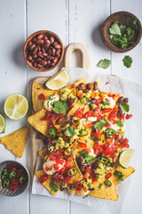 Nachos chips with cheese sauce, guacomole, salsa and vegetables on the board, top view. Party food concept.