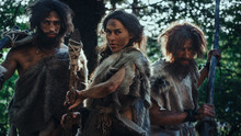 Female Leader And Two Primeval Cavemen Warriors Threat Enemy With Stone Tipped Spear, Scream, Defending Their Cave And Territory In The Prehistoric Times. Neanderthals / Homo Sapiens Tribe