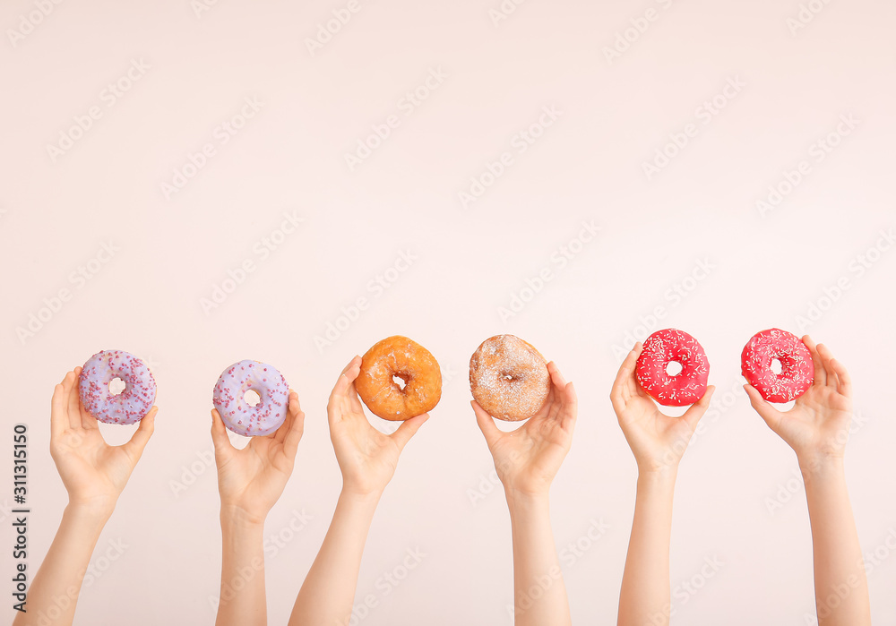 Female hands with sweet donuts on color background