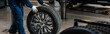cropped view of mechanic with car wheel in workshop, panoramic shot