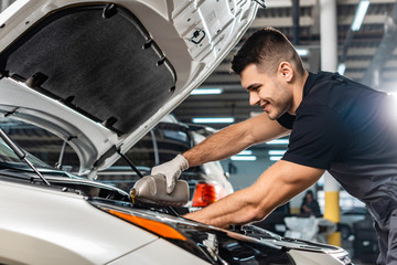 Wall Mural - smiling mechanic pouring motor oil at car engine