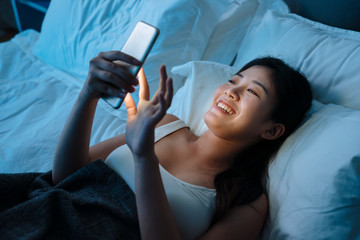 young beautiful asian japanese woman in bed using mobile phone late at night dark bedroom. happy girl lying in sleep place relax enjoy social media network at smartphone. internet addiction concept