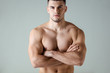 sexy muscular bodybuilder with bare torso posing with crossed arms isolated on grey