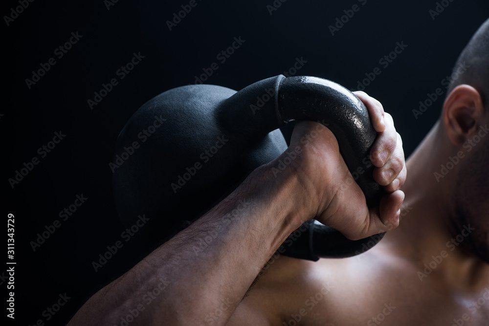 cropped view of muscular bodybuilder excising with kettlebell isolated on black - obrazy, fototapety, plakaty 