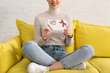 Wall Mural - Cropped view of smiling woman showing gift card on sofa