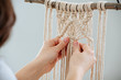 Craftswoman weving ropes, creating a macrame banner. from behind.