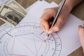 cropped view of astrologer drawing natal chart beside cash on table