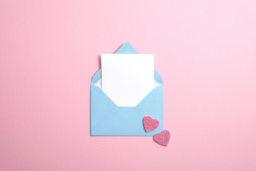 Blue envelope with blank white paper note inside and Valentines hearts on pink background. Romantic love letter for Valentine's day concept.