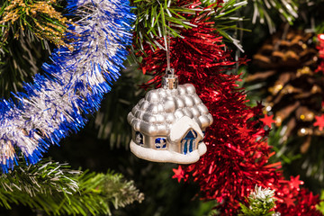 The christmas tree ornament toy, the little house or hut  on the fluffy artificial pine or fur branch with red and blue garland 