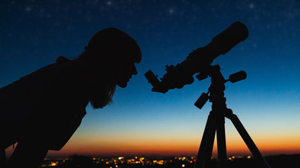 Wall Mural - astronomer with a telescope watching at the stars and moon with blurred city lights in the backgroun