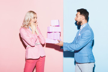 Wall Mural - handsome man giving gifts to shocked woman on pink and blue background