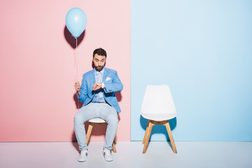 Wall Mural - nervous man holding balloon and looking at wristwatch on blue and pink background