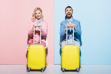 Wall Mural - smiling woman and handsome man holding travel bags on pink and blue background