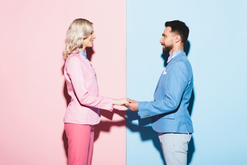 Wall Mural - side view of smiling woman and handsome man holding hands on pink and blue background