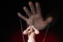Concept Of Control. Marionette In Human Hand. Objects Are Colored On Red And Blue Light.