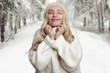 © Lars Zahner - Young blond woman enjoying her white knitted sweater, standing against winter forest landscape background, with her hands to her neck and smiling with eyes closed